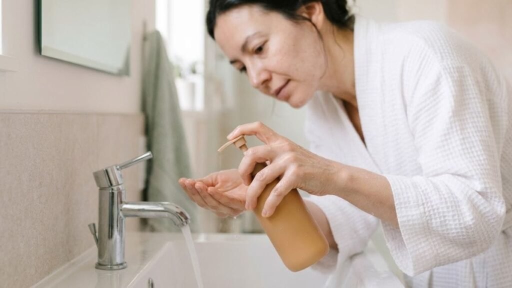 Hand with a plain cleanser bottle and warm water for a basic skincare routine for women